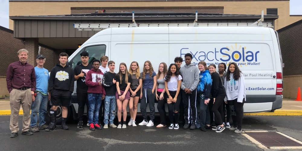 Exact Solar stands in front of their company van with school students to celebrate their donation to the school district