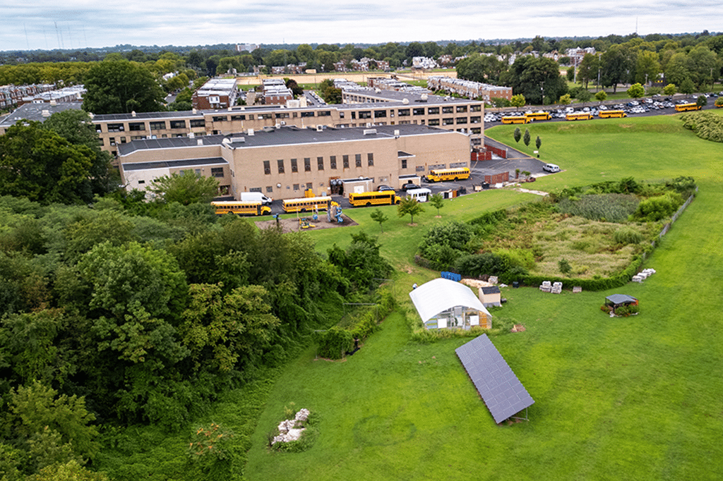 a school building with a parking lot and a parking lot with buses and a ground-mounted solar array