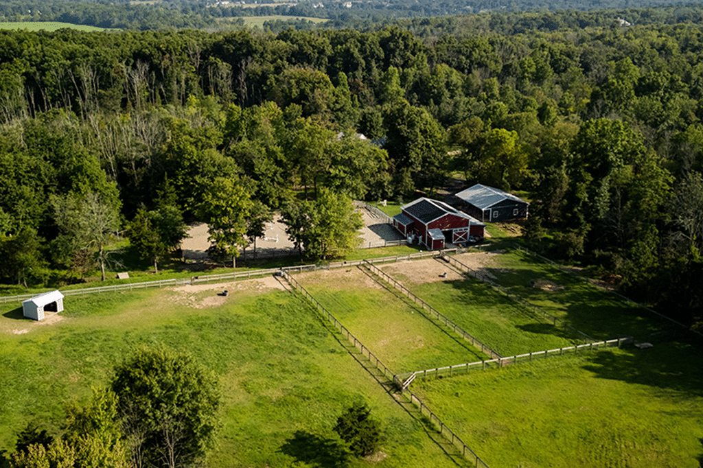 a farm with a fence, trees, and a barn with solar panels on the roof