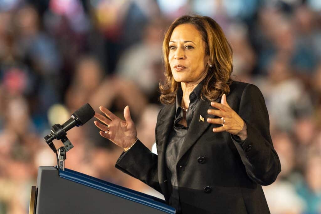 Kamala Harris standing at a podium with her hands up at a campaign rally